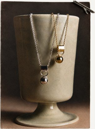 Two pendant necklaces displayed on a ceramic vessel